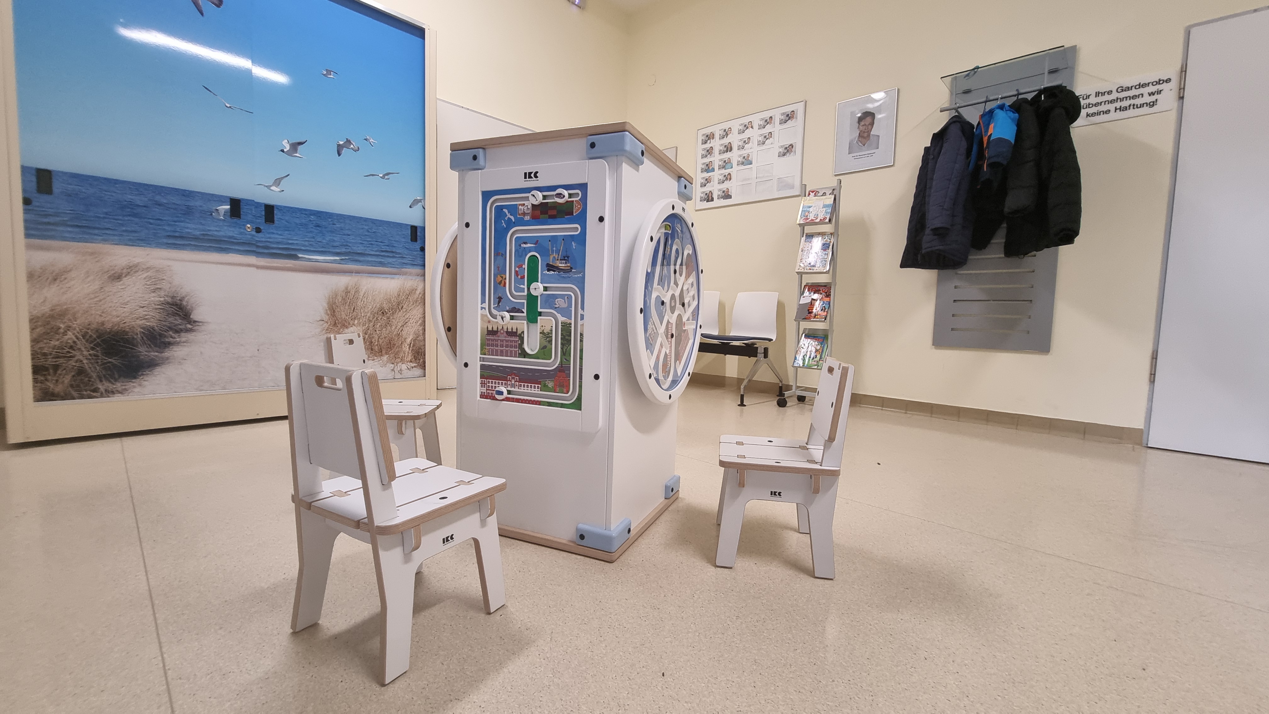 IKC speeltafel met interactieve wandspellen en kinderstoelen in de wachtruimte van Universitätsmedizin Rostock, ingericht met stranddecoratie.