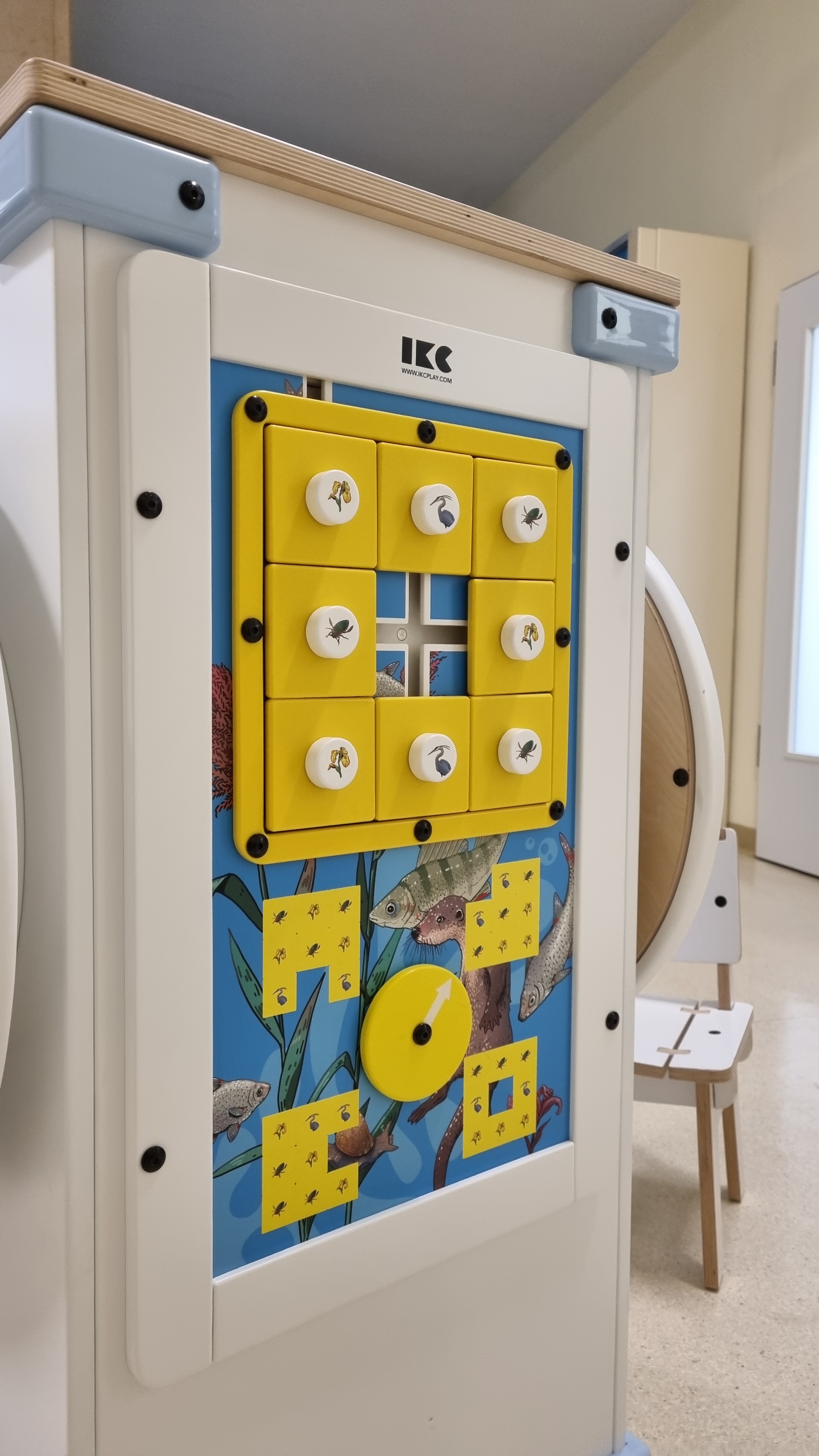 Interactief wandspel van IKC met gele draaiblokken en dierillustraties, geplaatst in de wachtruimte van Universitätsmedizin Rostock.