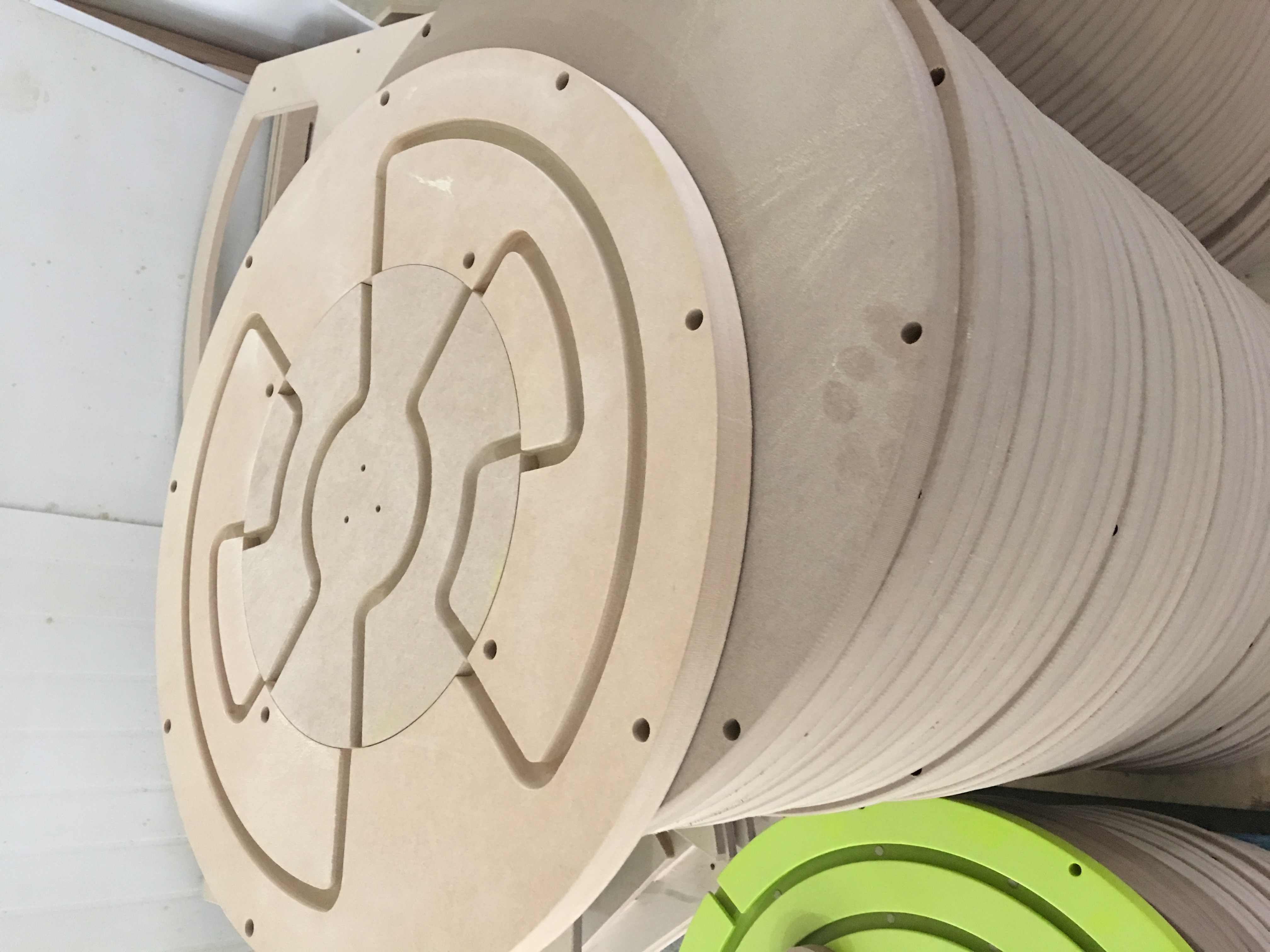 Gestapelde ronde houten panelen voor kinderspeeltoestellen tijdens productieproces bij IKC