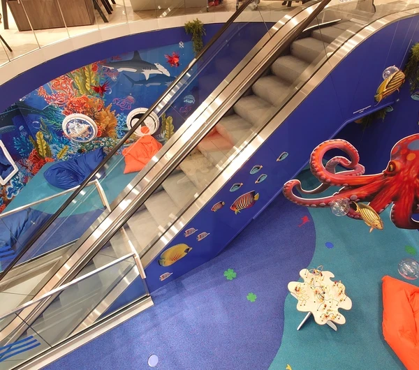 Speelhoek met onderwaterthema bij Modehaus Baltz, ingericht langs de roltrap met kleurrijke muurschilderingen van vissen, een grote octopus, interactieve wandspellen, zitzakken en een speeltafel