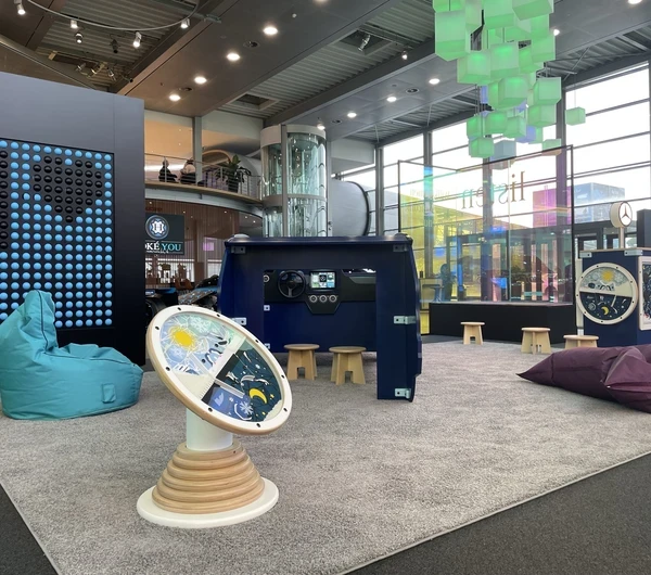 Kinderhoek in Mercedes-Benz Kundencenter met diverse speelobjecten, waaronder een blauw dashboard-speelmeubel, interactieve wandspellen, grote turquoise en paarse zitzakken en kleurrijke verlichting in een moderne showroomomgeving.