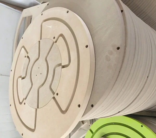 Gestapelde ronde houten panelen voor kinderspeeltoestellen tijdens productieproces bij IKC