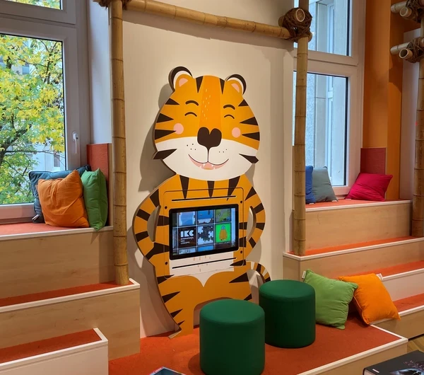 Espace enfants coloré avec un écran interactif intégré dans une borne en forme de tigre, installé dans la librairie Thalia à Krefeld.