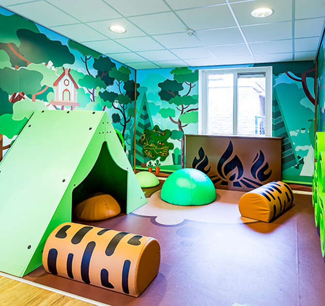 Inrichting kinderdagverblijf met een camping thema met wandspellen en softplay kussens en een tent