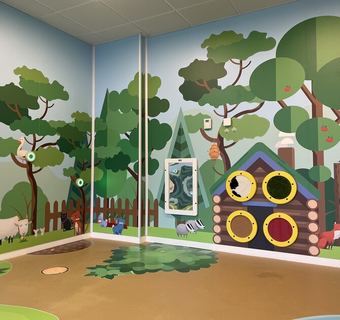 Interactive forest-themed children’s play corner with tactile wall elements, animal illustrations and activity panels
