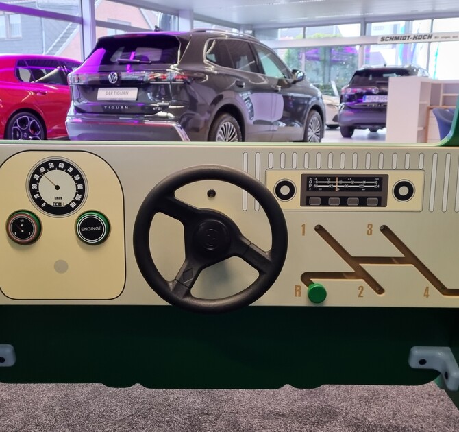 Binnenkant van de op maat gemaakte groene IKC VW-speelbus in de showroom van Autohaus Schmidt + Koch, met een stuur, snelheidsmeter en versnellingspook, ontworpen voor spelend leren en klantbeleving.