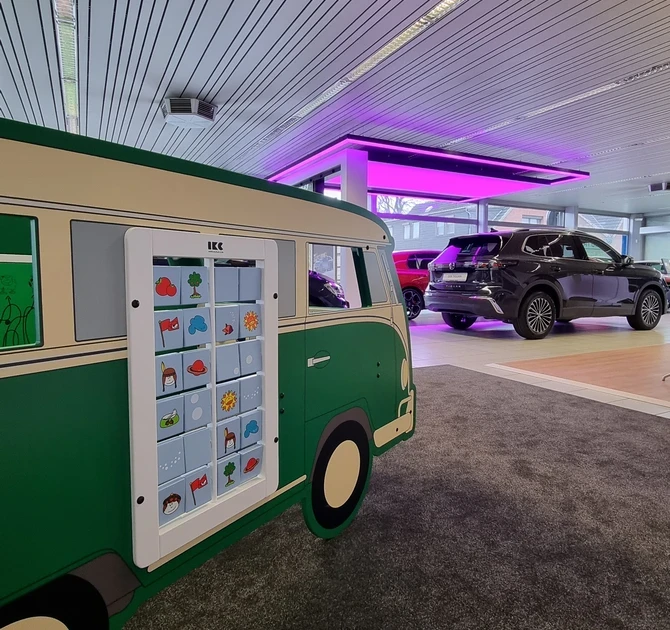 Groene IKC speelbus met flippaneelwand in Volkswagenstijl, geplaatst op tapijt in een moderne showroom met diverse auto’s op de achtergrond en opvallende paarse verlichting.