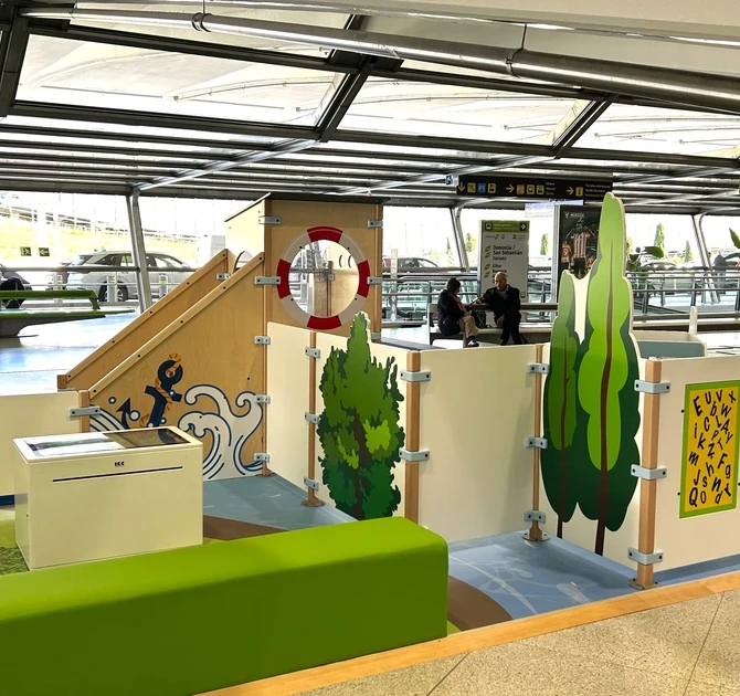 "Kindvriendelijke speelhoek op Bilbao Airport met maritiem thema, inclusief klimelementen, interactieve spellen en zitbank voor ouders in een lichte vertrekhal."
