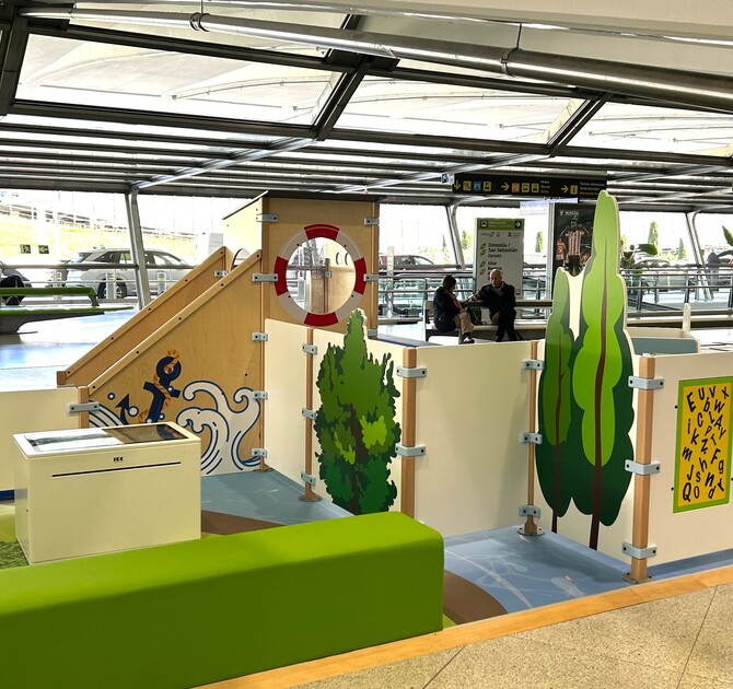 "Kindvriendelijke speelhoek op Bilbao Airport met maritiem thema, inclusief klimelementen, interactieve spellen en zitbank voor ouders in een lichte vertrekhal."
